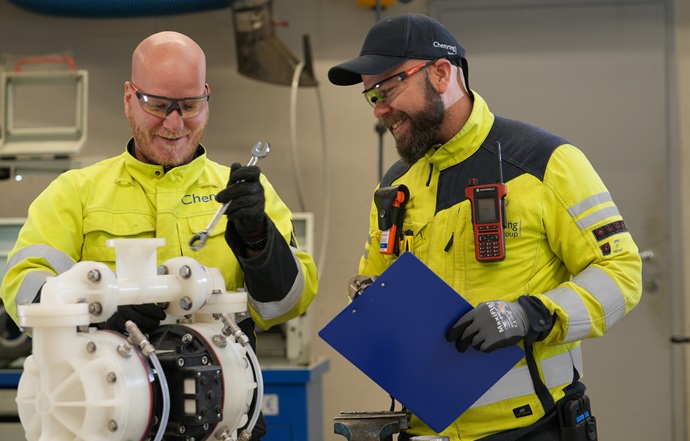 two employees in high vis jackets and safety equipment working on machinery